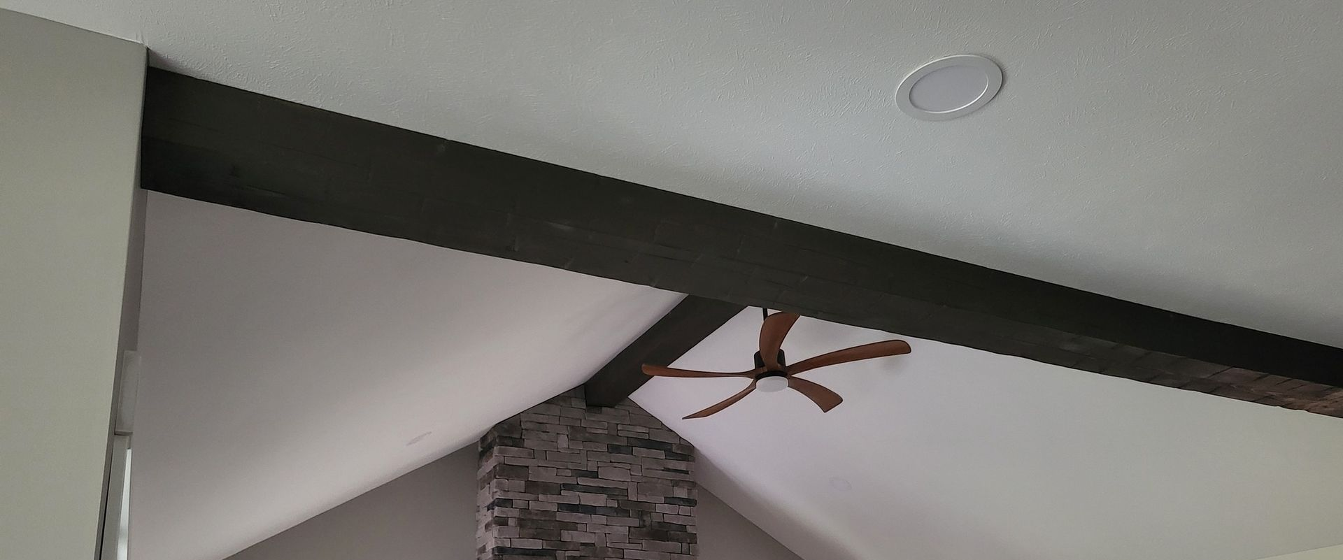 Ceiling fan under a slanted white ceiling with a stone chimney accent.