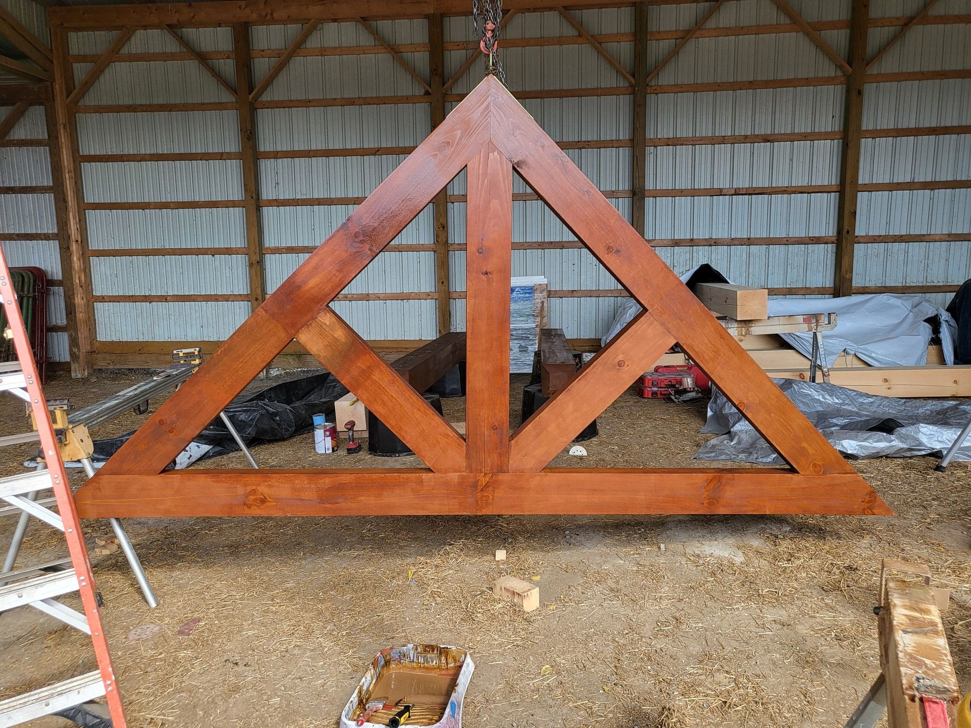 Wooden triangular truss structure in a workshop, with tools and materials around it.