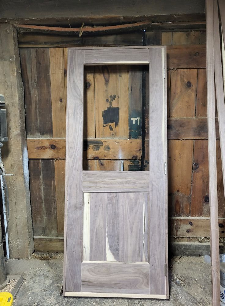 Gray unfinished door leaning against a weathered wooden wall in a rustic workshop