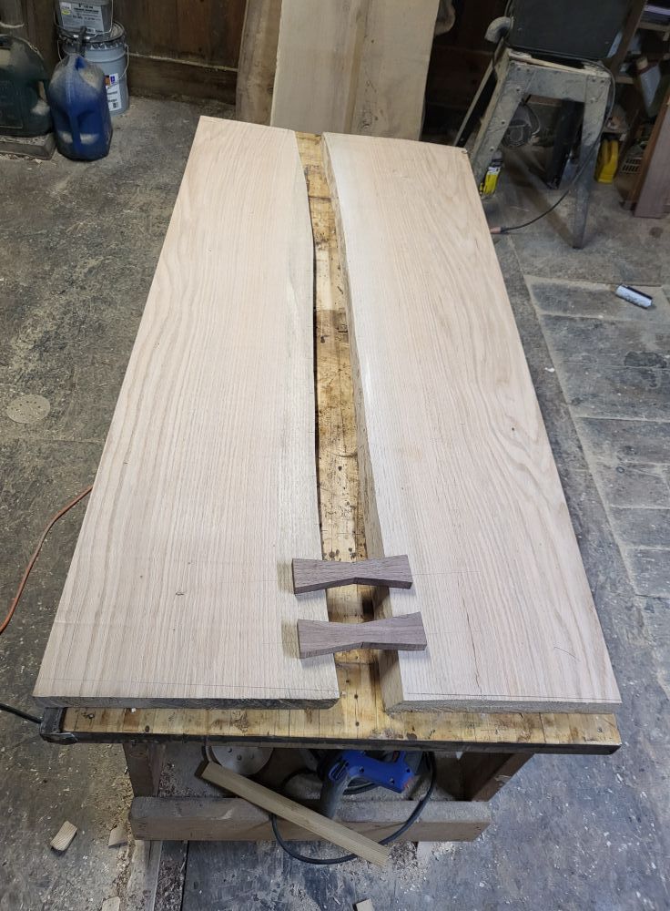 Two light wood slabs on a workbench with a rough bark strip between them in a workshop