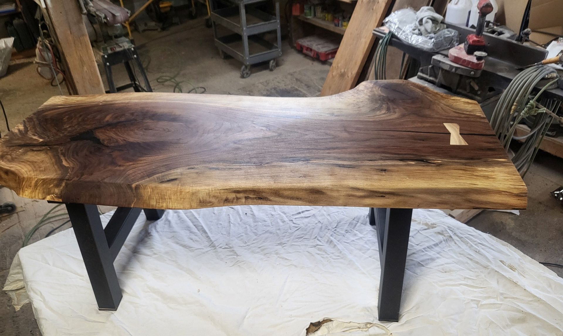 Live-edge wooden table top on black metal legs in a workshop, with a dark brown finish.