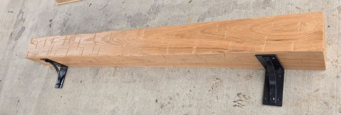 Long wooden shelf mounted on a textured gray wall with black metal brackets