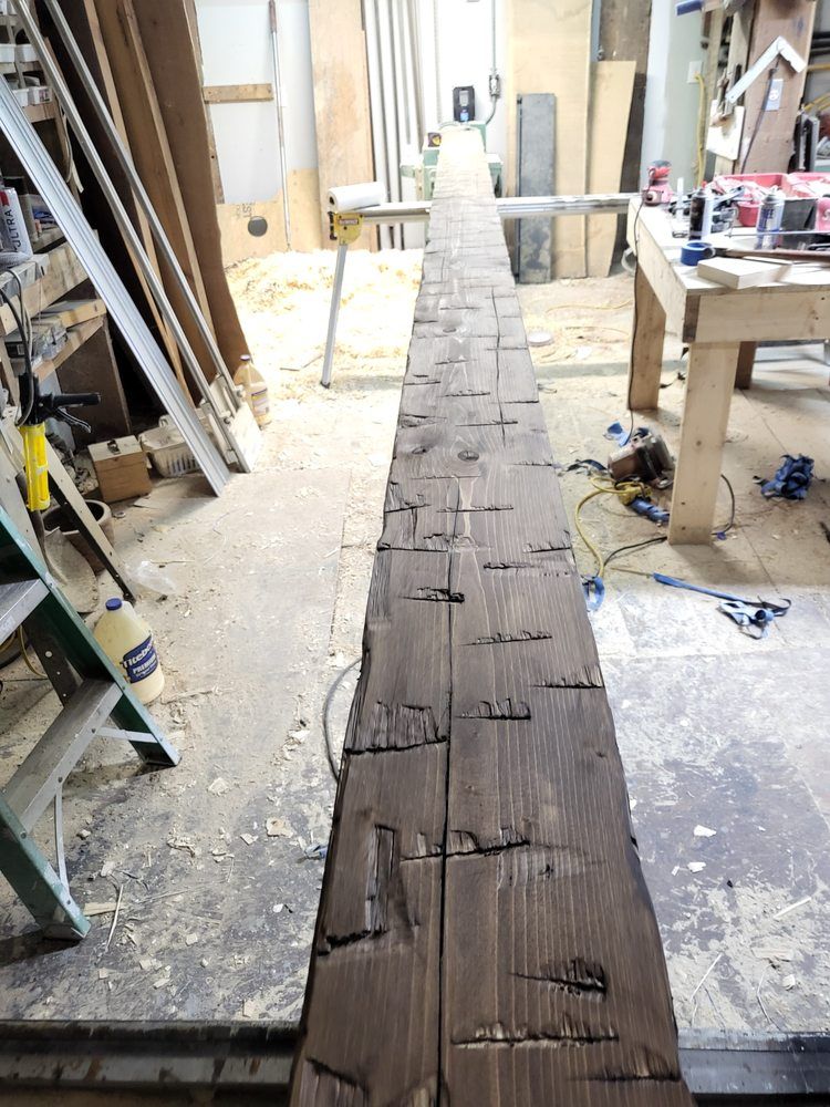 Long weathered wooden beam in a cluttered workshop, viewed from above.