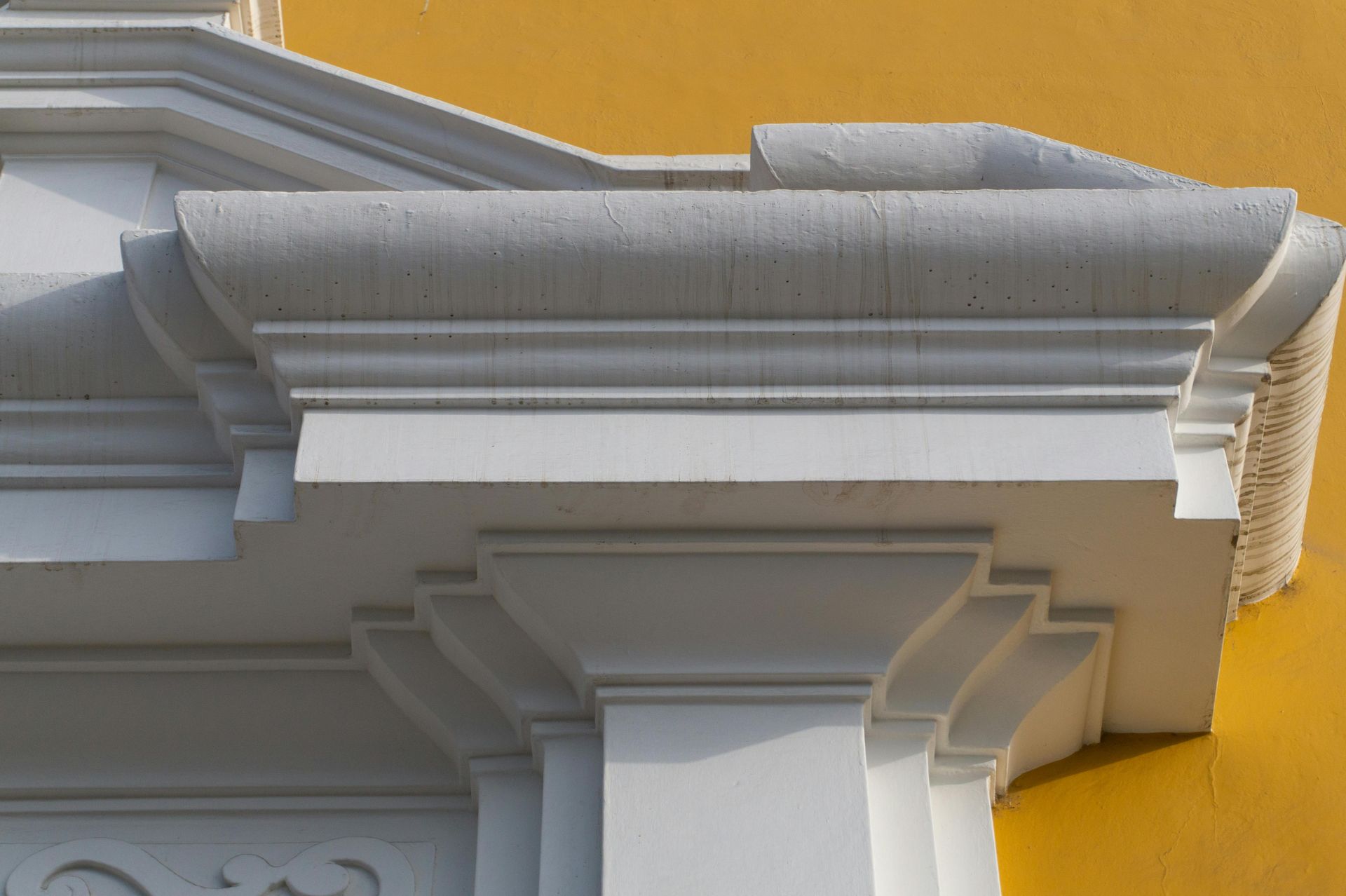 White ornate roof cornice and columns against a bright yellow wall
