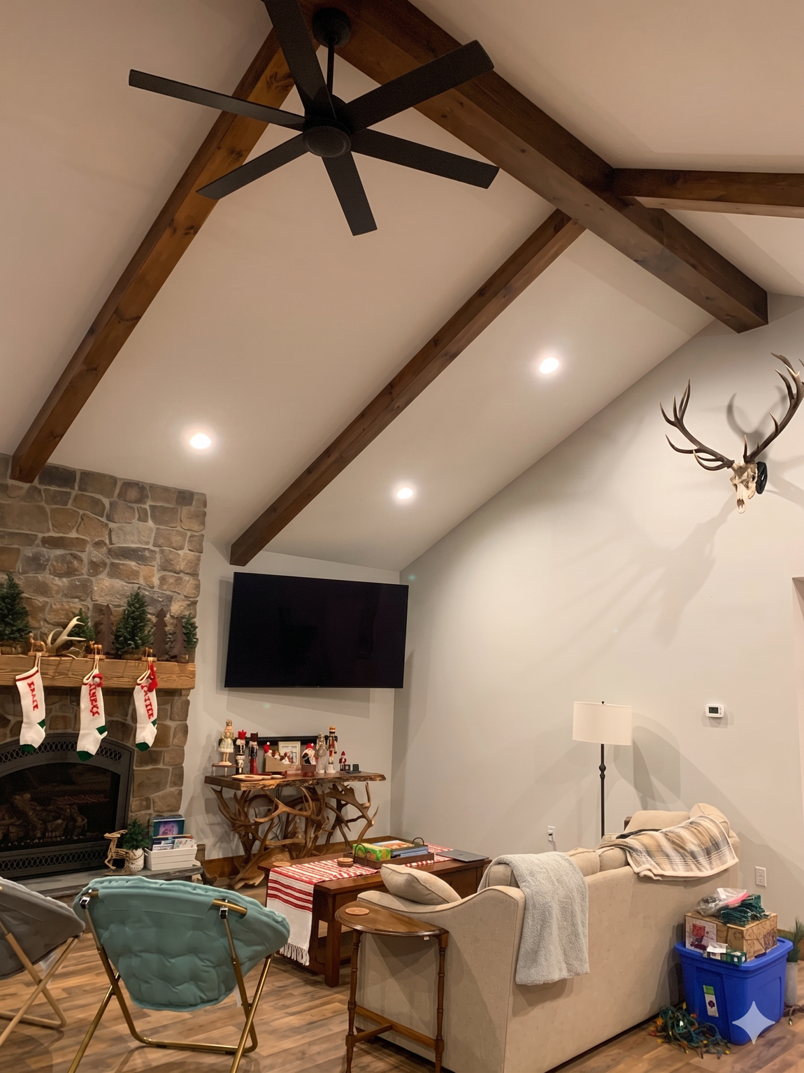 Cozy living room with vaulted wood beams, stone fireplace, wall-mounted TV, and beige sectional sofa