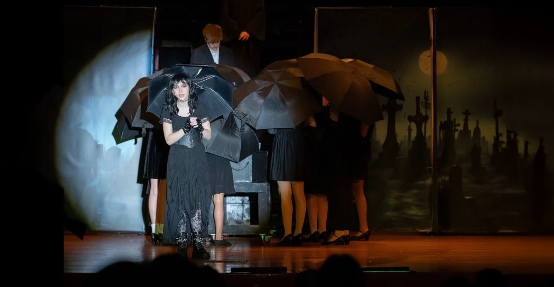 People under umbrellas gathered on a dim stage with blue and orange lighting.