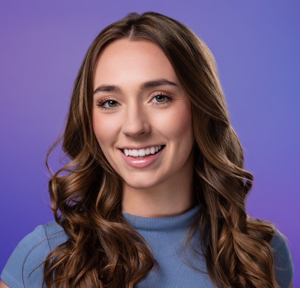 Smiling woman with wavy brown hair against a purple background