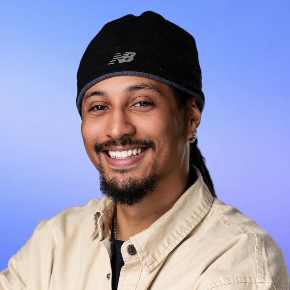 Smiling person in a black beanie and beige jacket against a blue background