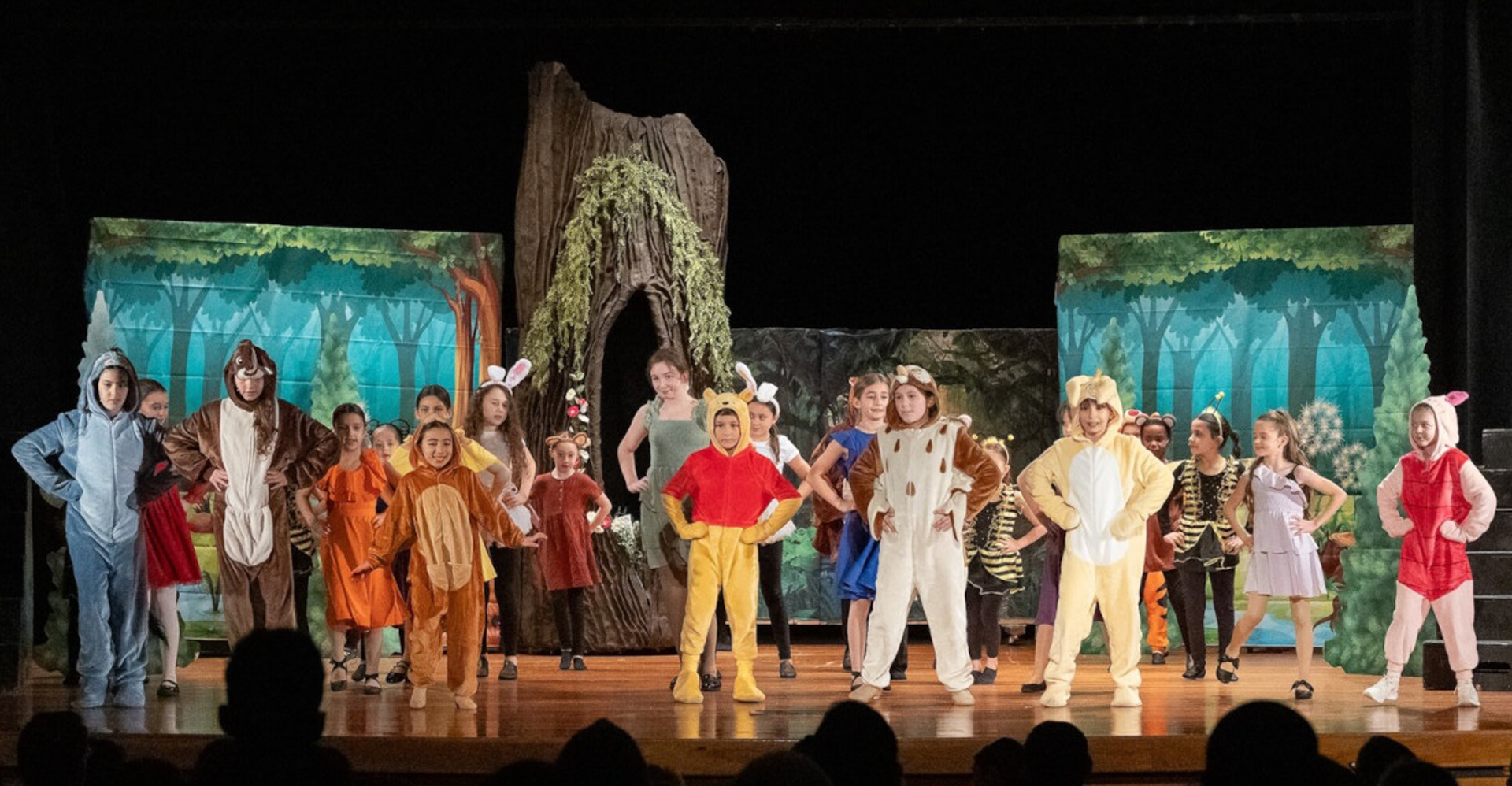 Costumed performers line up onstage in front of painted jungle scenery during a theatrical performance.