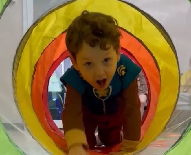 Child crawling through a colorful fabric tunnel, mouth open, in a playful indoor setting