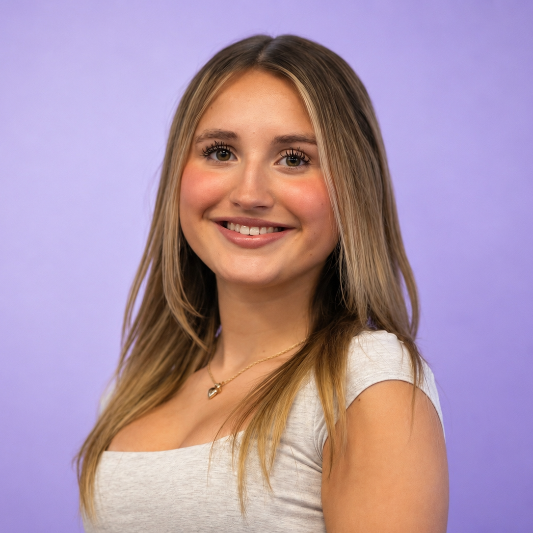 Smiling person with long highlighted hair wearing a white top against a purple background