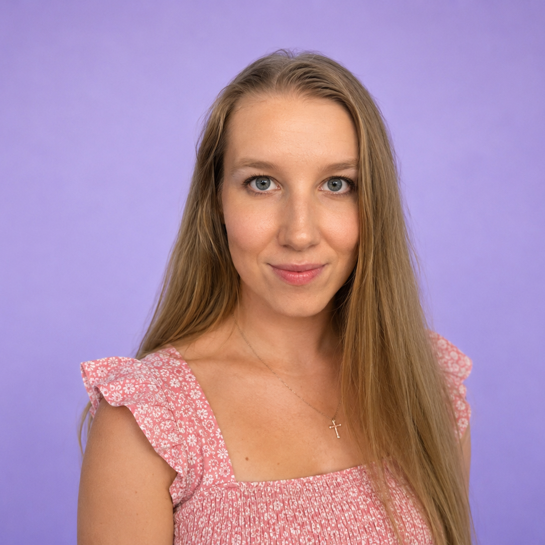 Smiling person with curly hair and glasses wearing a black shirt against a purple background