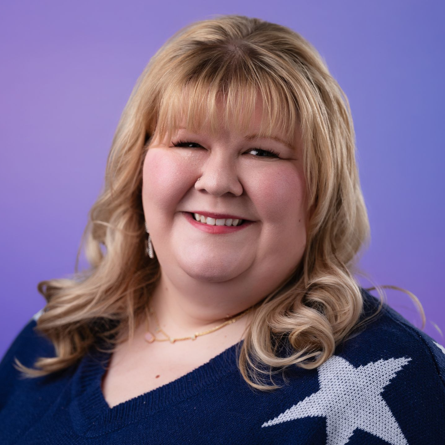 Smiling woman in a navy sweater with white stars against a purple background