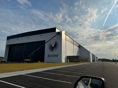 Large white industrial building with BOOM logo beside an empty road under a cloudy sky