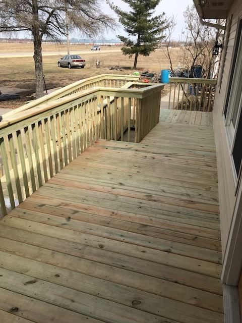 Wooden deck with railings overlooking a yard and parked car on a cloudy day