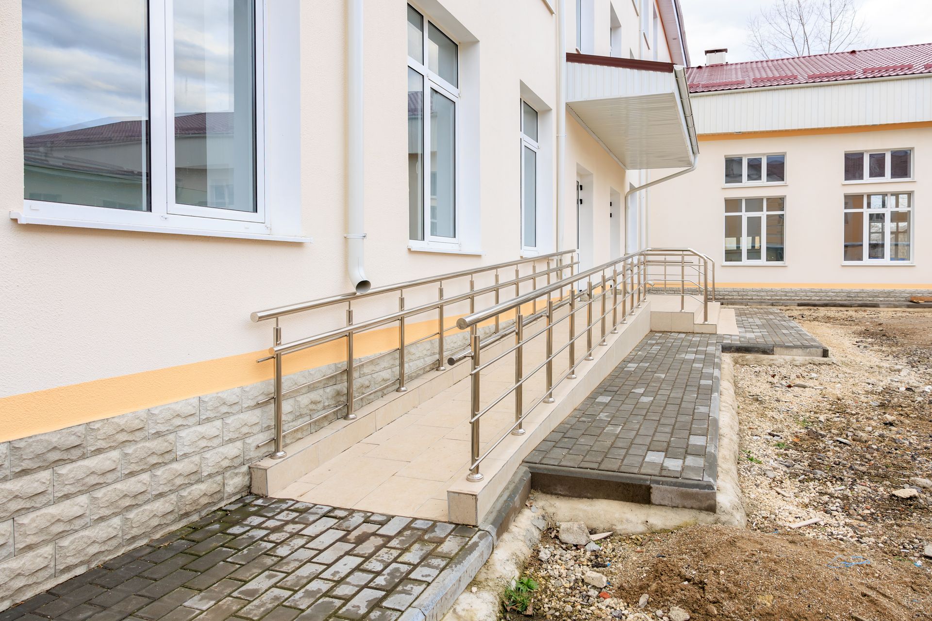 Ramped entrance beside a white building with metal handrails and cobblestone paving Ramped entrance beside a white building with metal handrails and cobblestone paving