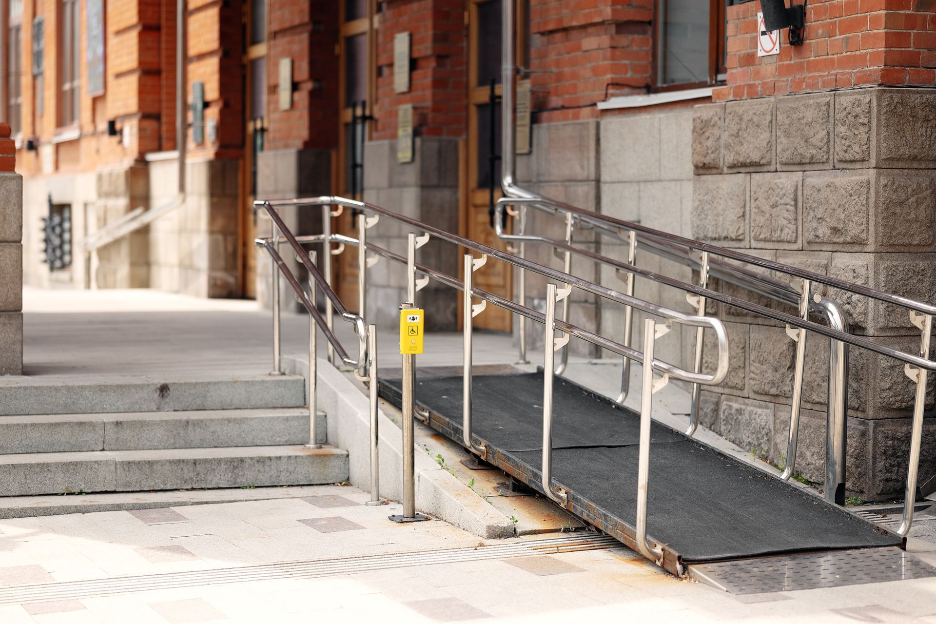 Outdoor wheelchair ramp with metal railings beside stone steps at a brick building entrance Outdoor wheelchair ramp with metal railings beside stone steps at a brick building entrance