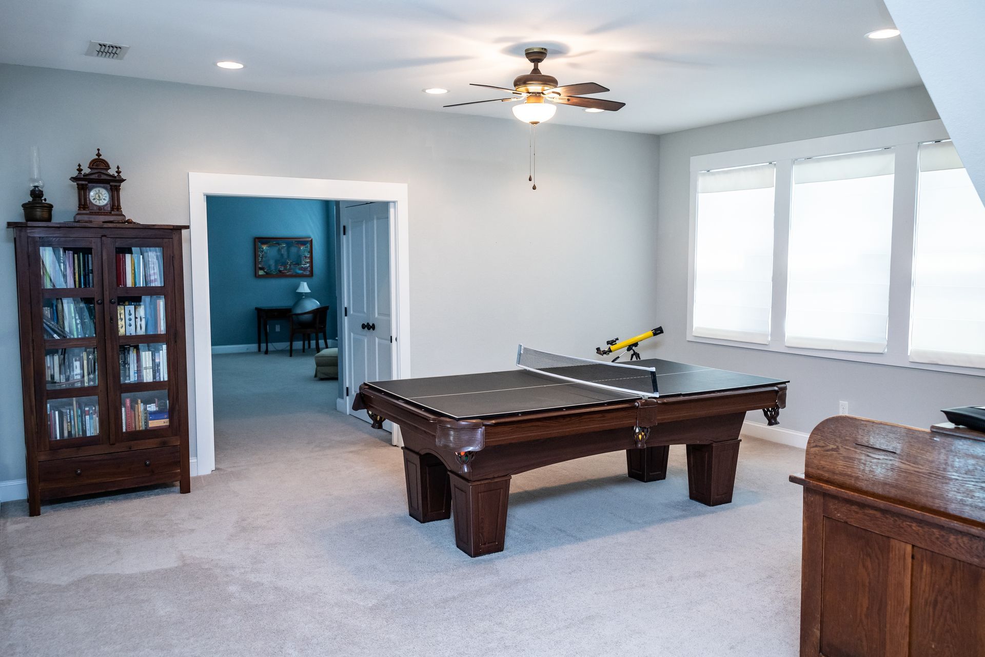 Bright game room with pool table, ceiling fan, bookshelf, and large windows. Bright game room with pool table, ceiling fan, bookshelf, and large windows.