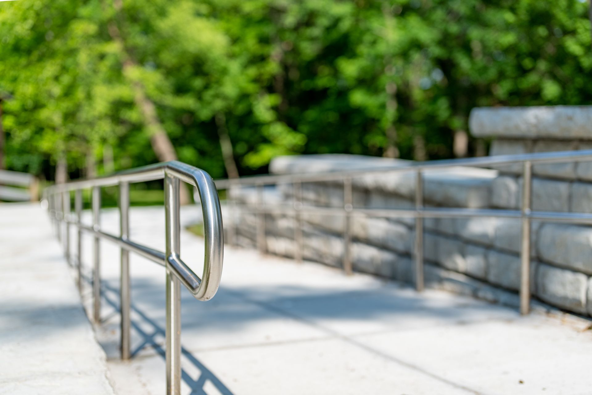 Metal handrails along a concrete ramp beside a stone wall and green trees Metal handrails along a concrete ramp beside a stone wall and green trees