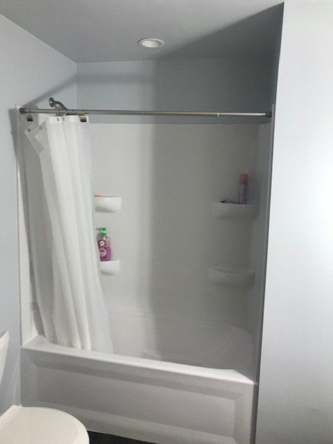 Small white bathtub with a shower curtain, tiled walls, and built-in corner shelves in a bathroom.