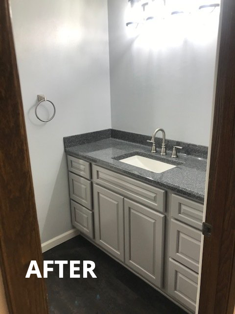 Small bathroom vanity with gray countertop, sink, and white cabinets against white walls.
