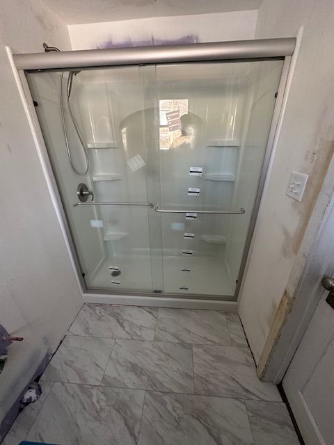 Walk-in shower with glass sliding door and marble-pattern tile floor in a bathroom.