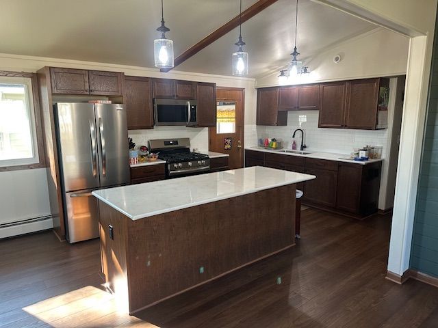 Modern kitchen with a large island, stainless steel appliances, dark wood cabinets, and pendant lights
