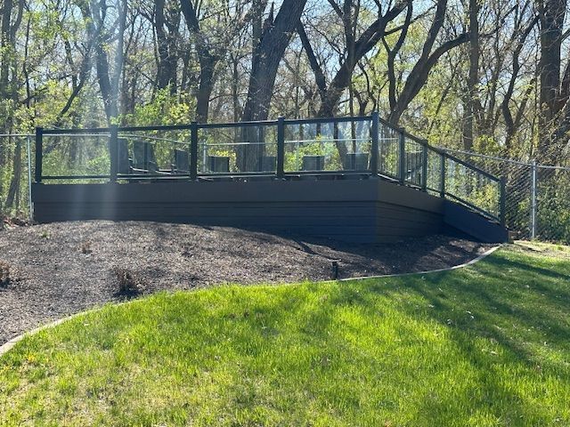 Modern black-railed deck on a grassy hillside in a wooded park.