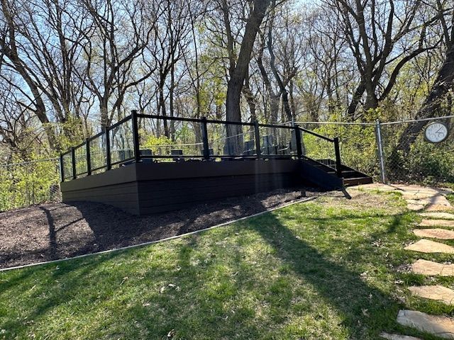 Black metal viewing platform on a grassy slope in a wooded park with steps and railings