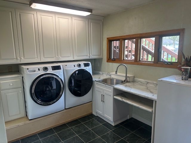 Laundry room with front-loading washer and dryer, white cabinets, sink, and green tile floor