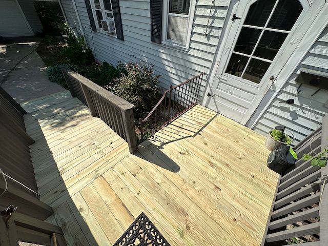Wooden deck with stairs, railing, and a white house exterior in sunlight