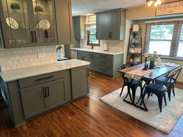 Modern kitchen with gray cabinets, white countertops, subway tile, and a wooden dining table by the window