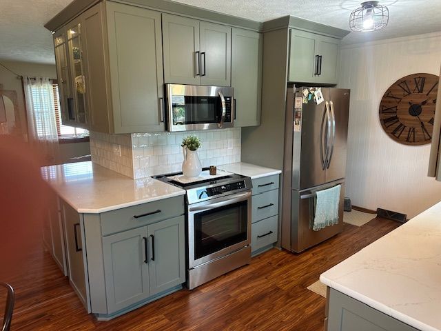 Modern kitchen with gray cabinets, stainless appliances, white countertops, and hardwood floors