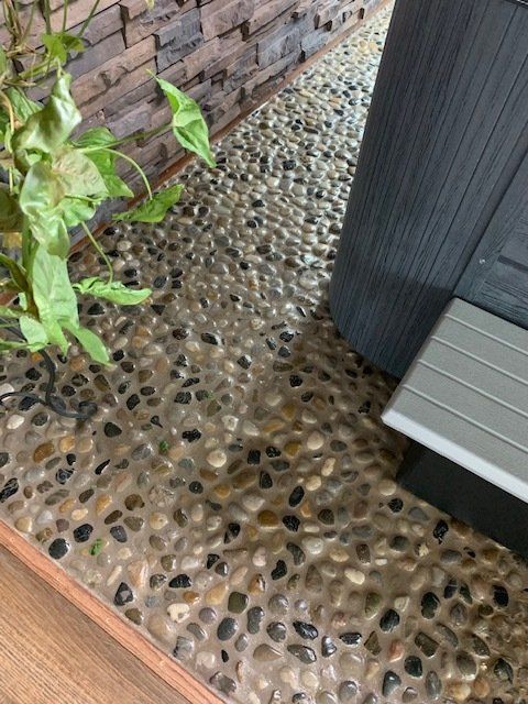Pebble-stone patio beside a brick wall and a black outdoor cabinet, with a green plant at left.