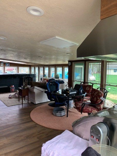 Living room with large windows, wood floors, and assorted furniture, including massage chairs and a sofa.