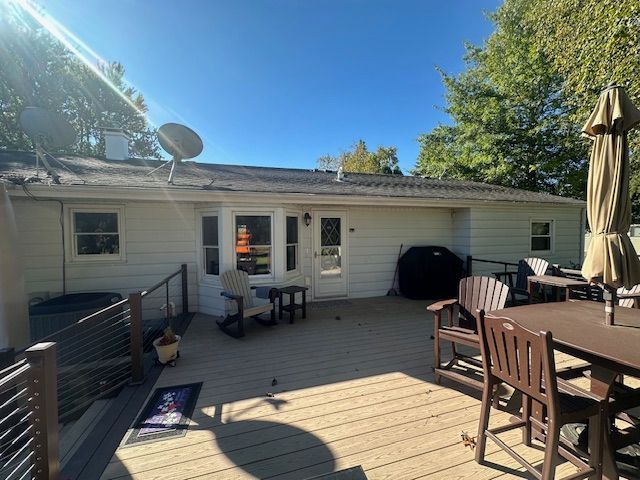 Sunny backyard deck with table, chairs, grill, and patio umbrella beside a white house