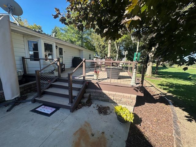 Backyard deck with wooden steps, railing, and a ramp beside a house under a tree.
