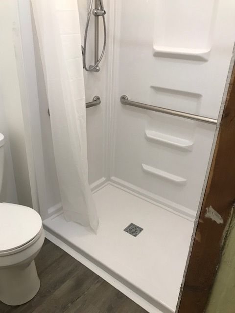 Small bathroom with a white shower stall, curtain, toilet, and dark wood floor.