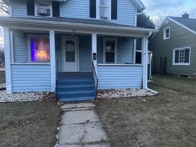 Blue house with a lit purple window, front porch, and concrete walkway at dusk