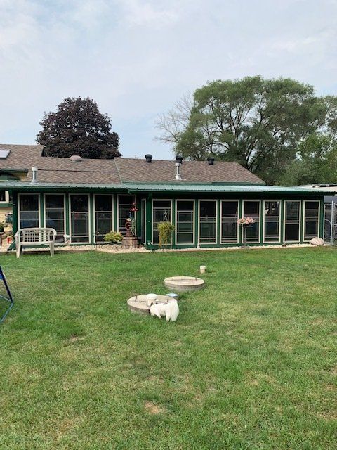 Backyard with a long green house, lawn, and a stone fire pit under cloudy skies