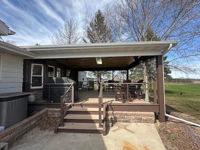 Covered backyard deck with steps, railing, and outdoor seating beside a house on a sunny day