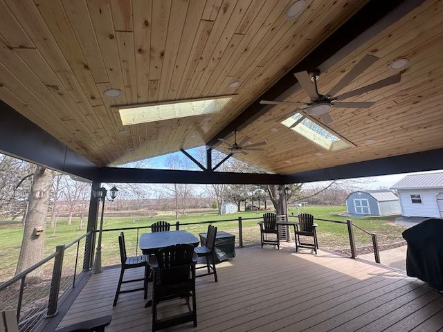 Covered backyard deck with wooden ceiling, string lights, outdoor table, chairs, and a grill overlooking a grassy yard