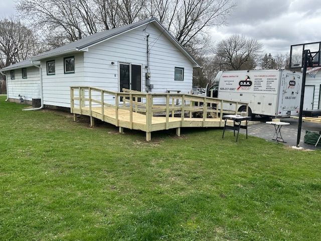 Single-story white house with a wooden ramp and deck in a grassy yard under cloudy skies