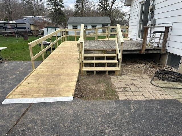 Wooden wheelchair ramp with handrails leading to a house porch over gravel and pavement