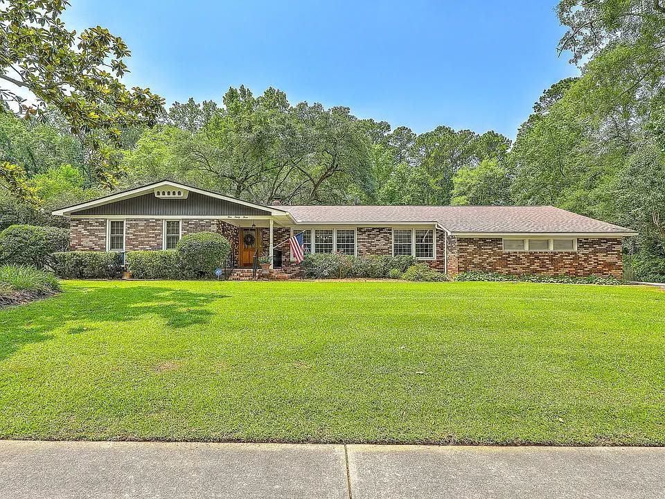 Single-story brick house with a wide front lawn and trees in the yard