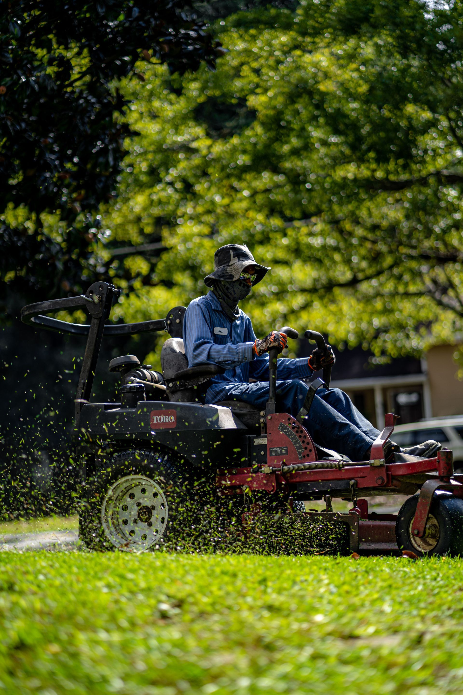 Person mowing a grassy lawn on a riding mower near trees and a fence