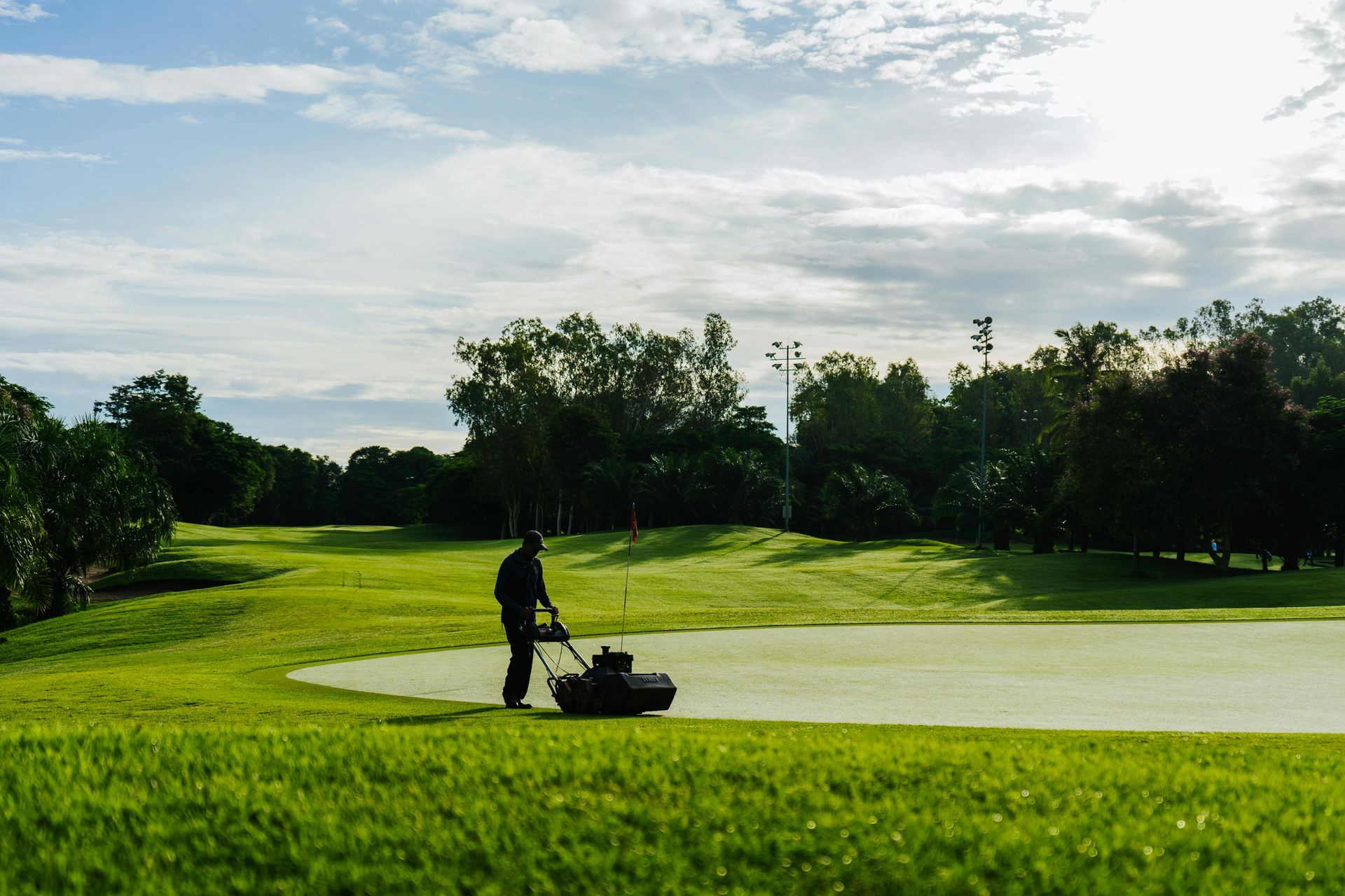Golfer silhouetted on a green under a bright sky with trees in the background