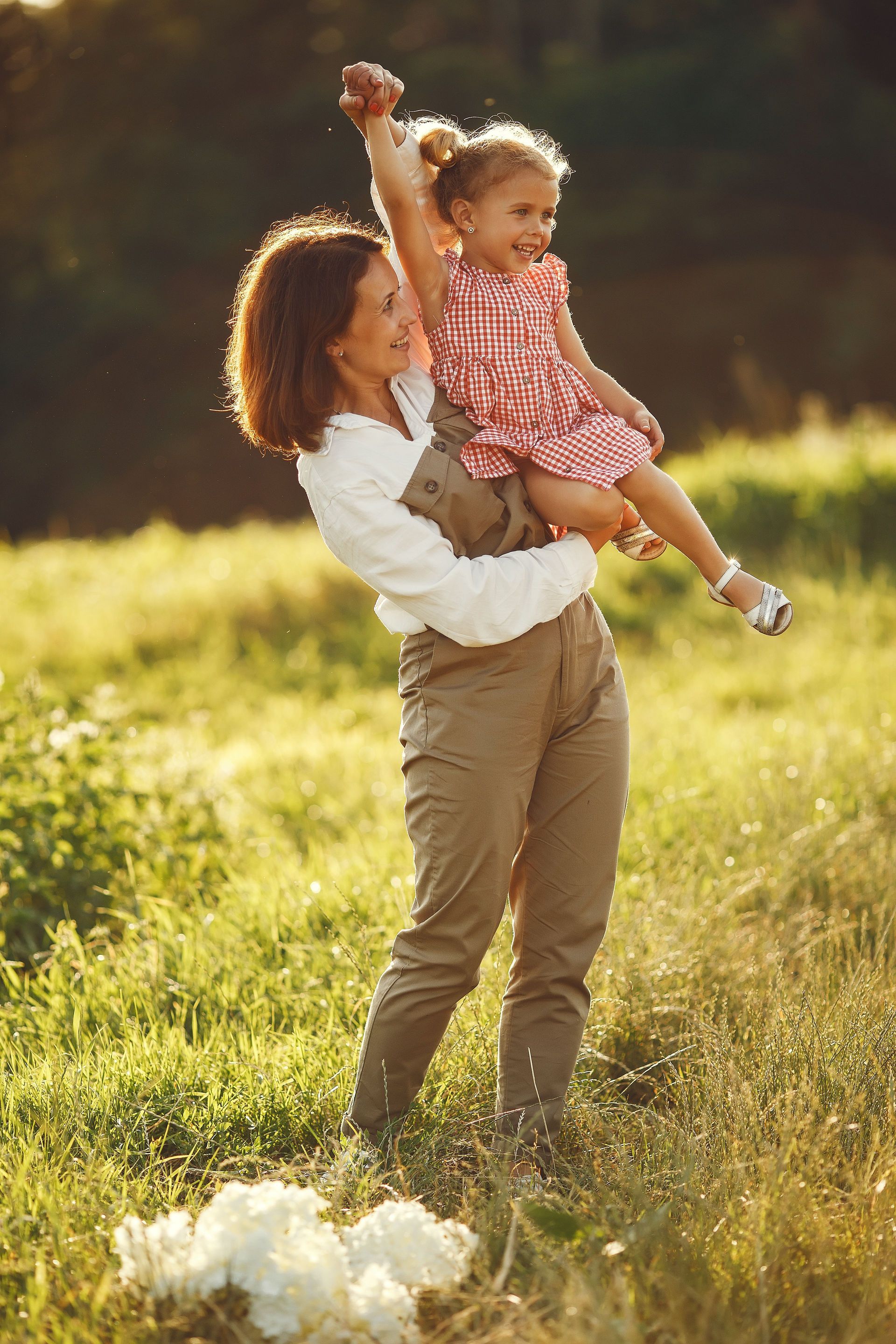 Woman lifting a smiling child in a sunlit grassy field