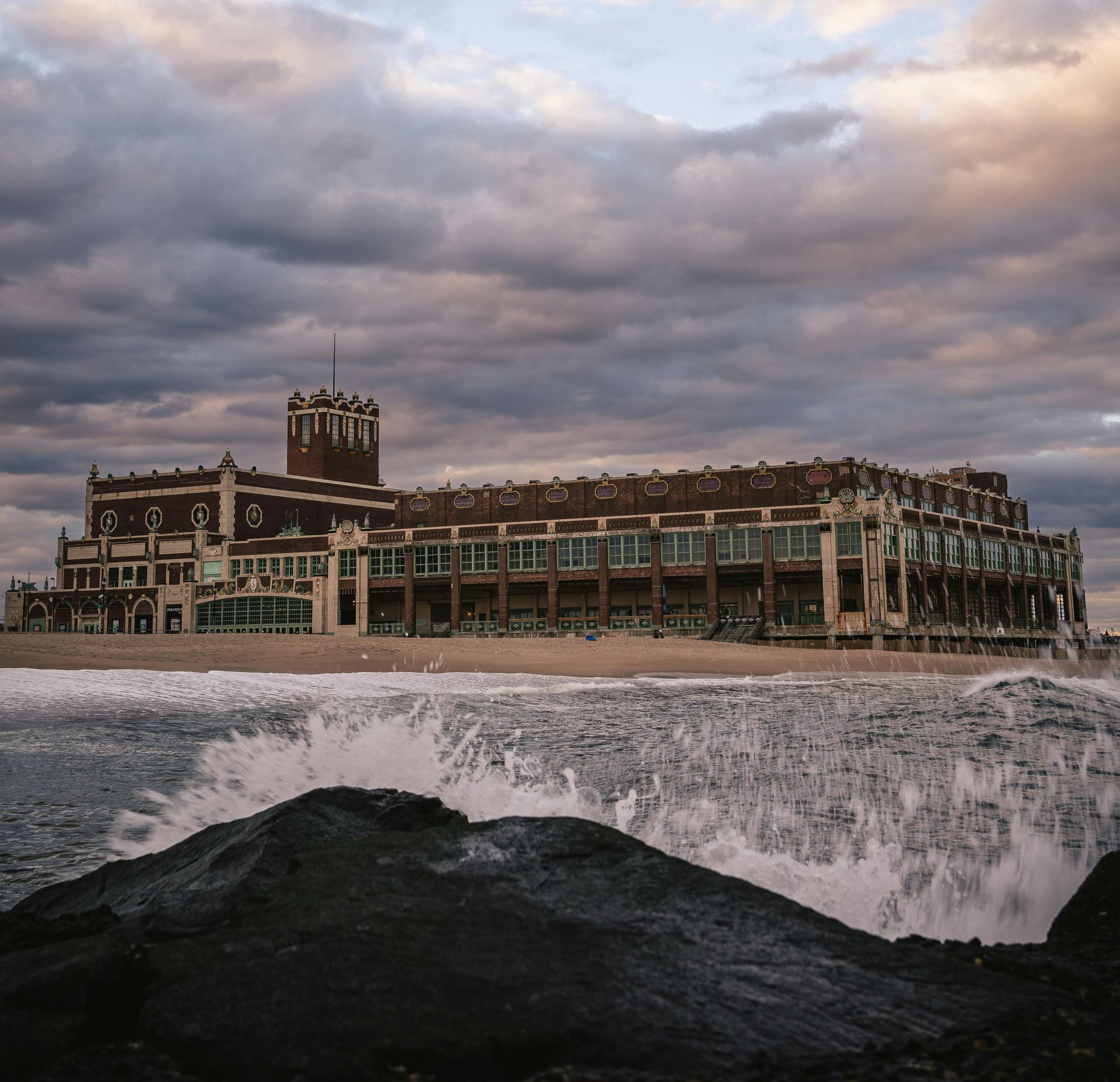 Large brick building on a beach, waves crashing, dark stormy sky overhead.