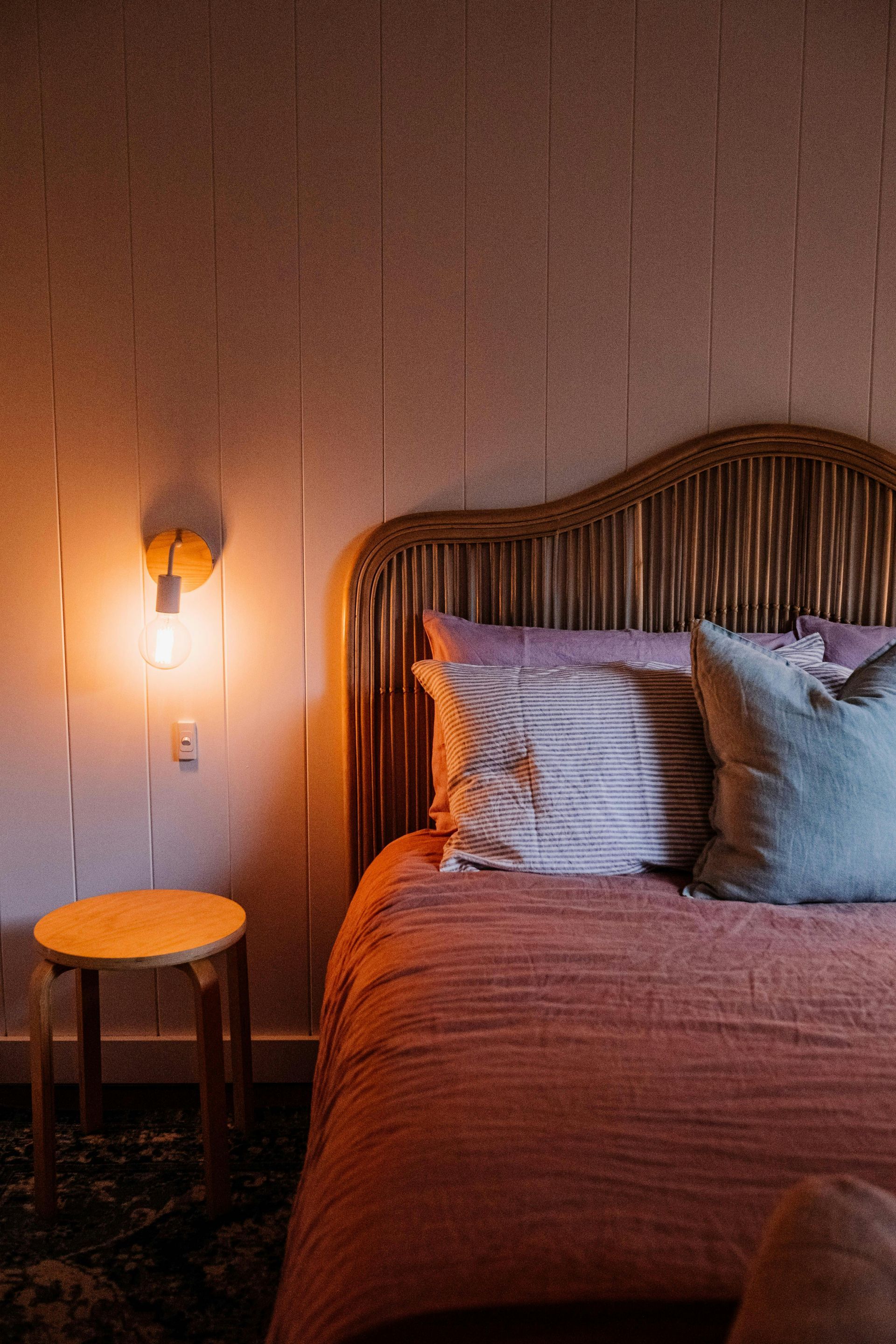 Bedroom with a woven headboard, pink bedding, and a glowing wall sconce.